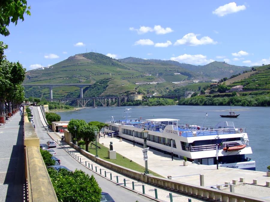 Peso da Régua riverside promenade and quay with a moored river-cruise boat, the Douro and terraced hills behind